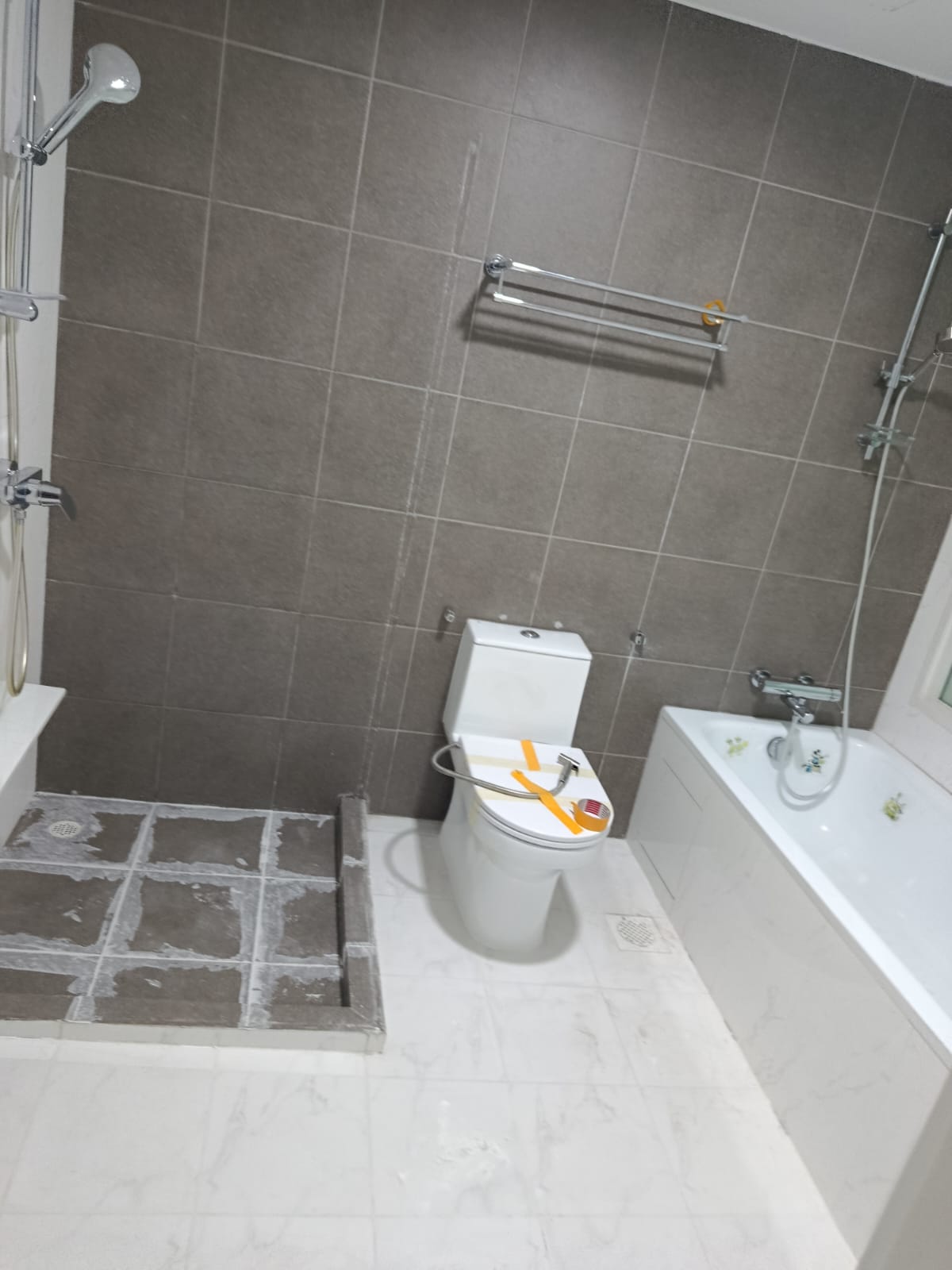Before: Condo bathroom with dark grey wall tiles, white marble floor, shower area with hacked tiles